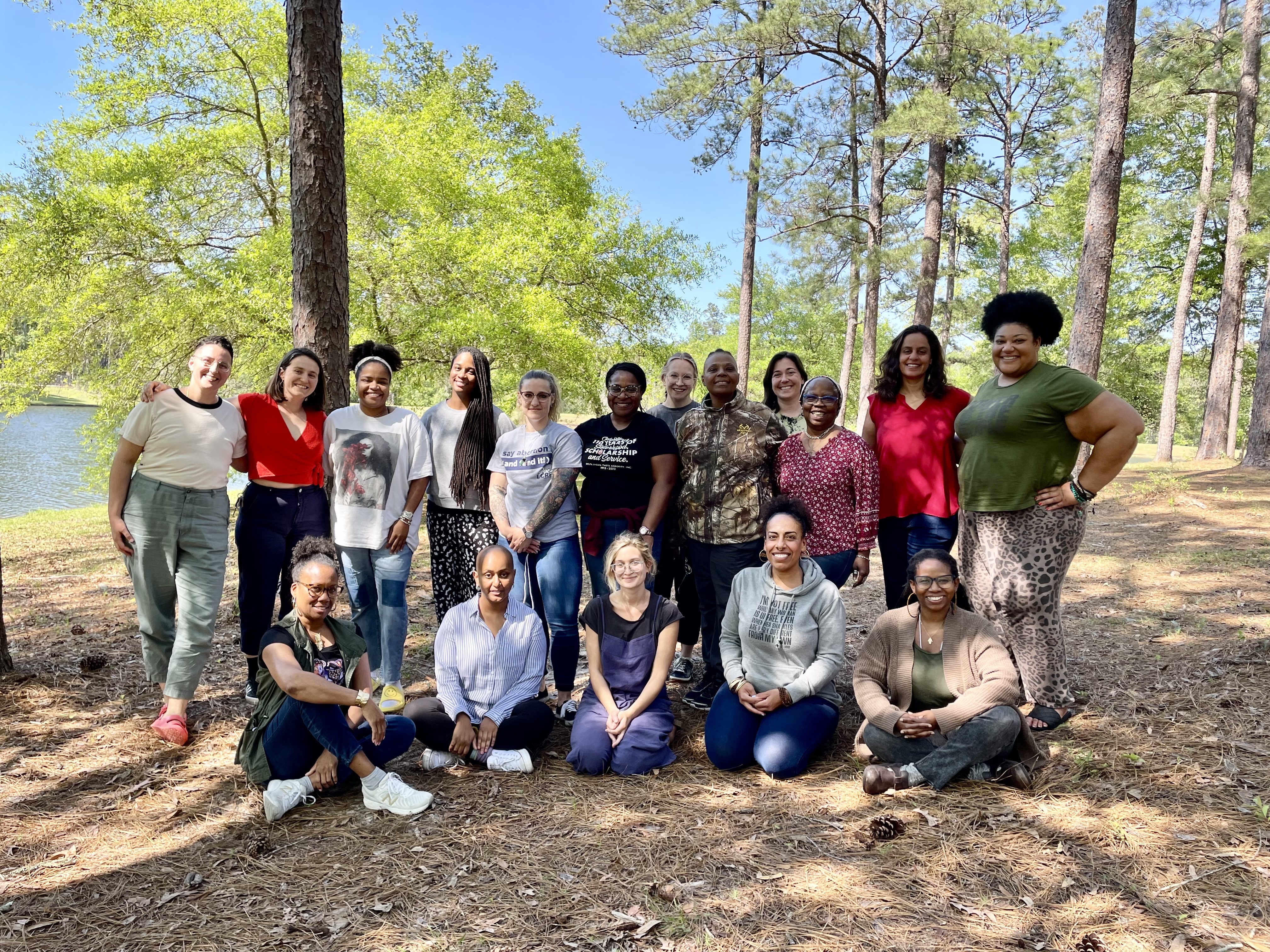 Participants of the 2023 HIVE Program. A multiracial group of 17 leaders in two rows in a wooded setting. A row of 12 leaders stands in the back and 5 leaders crouch in front of them, all smiling at the camera.